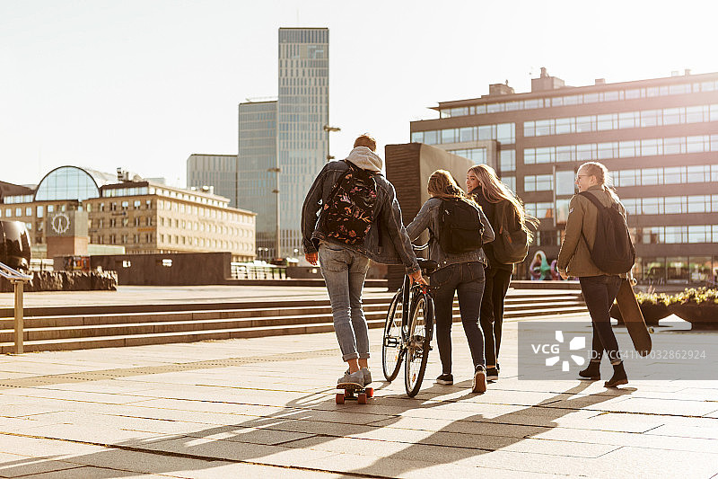 后视图的朋友与自行车和滑板在步行区在城市对天空图片素材