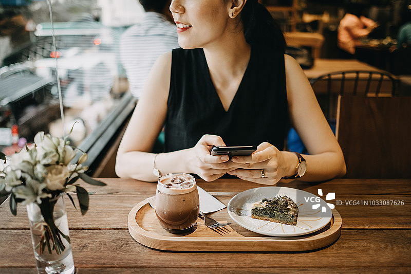一个女人在咖啡馆用智能手机享受咖啡和蛋糕图片素材