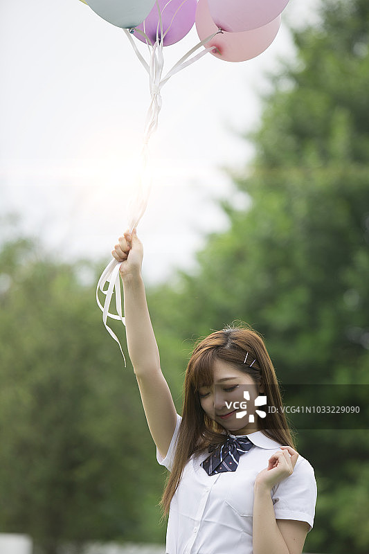 夏天五颜六色的气球。年轻的成年亚洲女孩举着一束彩色气球站在公园里的肖像。图片素材
