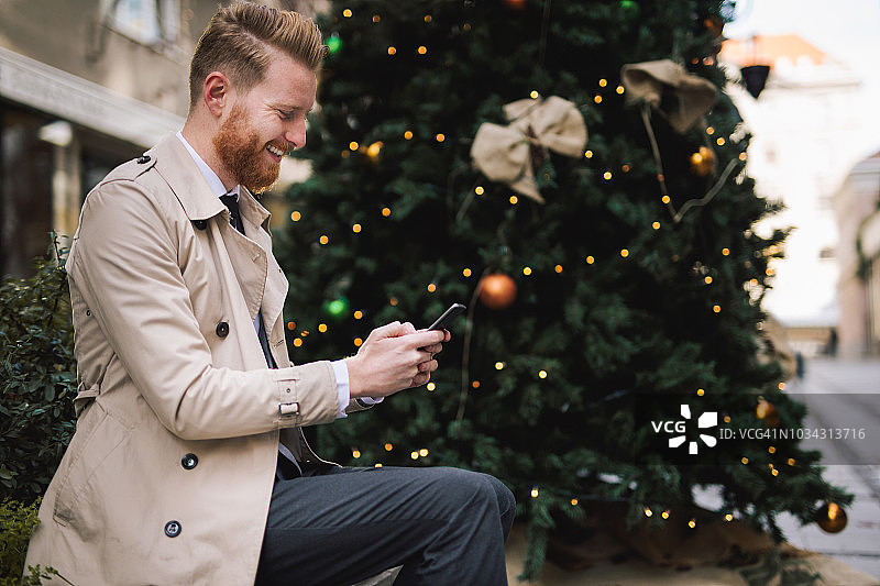 长着胡子的漂亮商人在圣诞树旁发短信图片素材