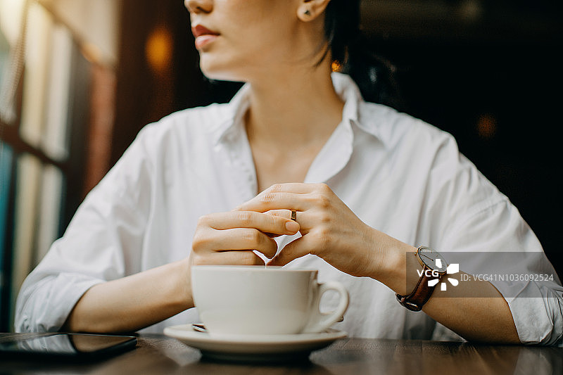 在咖啡厅喝咖啡和等待的时候，一个女人紧张地触摸着她手指上的结婚戒指图片素材