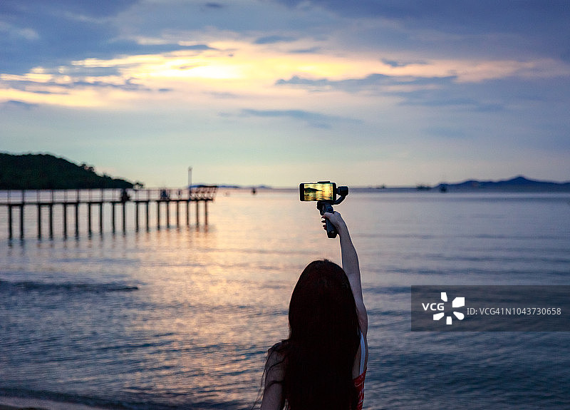 女人拍照和拍摄与智能手机在海滩黄昏日落的观点图片素材