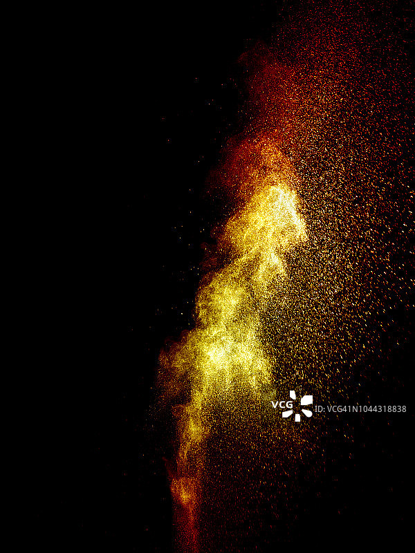 一团红色和黄色的粉末颗粒在黑色的背景上受到冲击而爆炸。图片素材