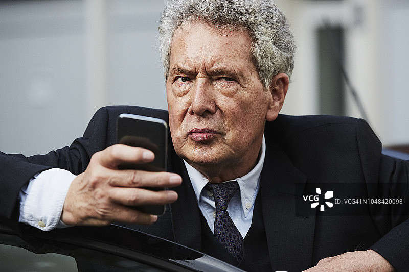 一位老人站在车旁查看智能手机的照片图片素材