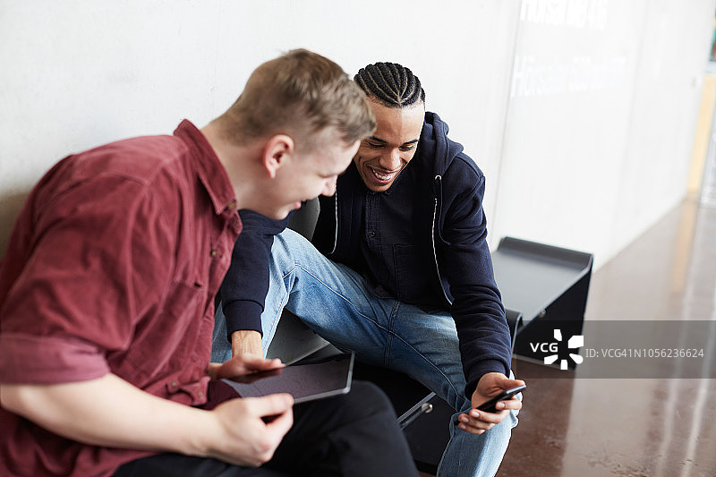 坐在大学长椅上微笑的男子向朋友展示手机图片素材