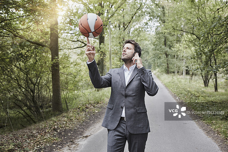 商人平衡篮球和通话在乡村道路上的智能手机图片素材