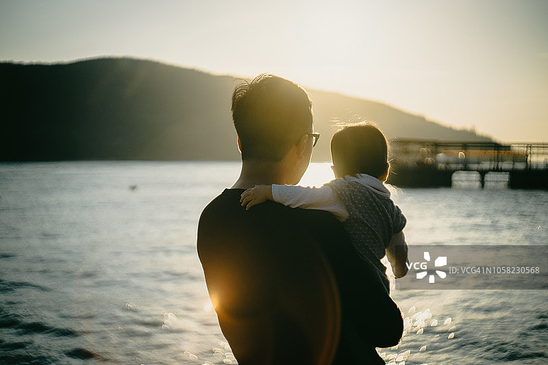 夕阳西下的海滩上，父亲抱着女儿图片素材