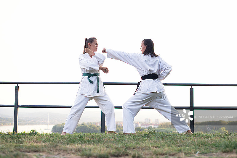 两个健康的年轻妇女穿着白色和服训练空手道武术在自然界。图片素材
