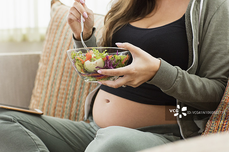 年轻孕妇坐在沙发上吃沙拉图片素材