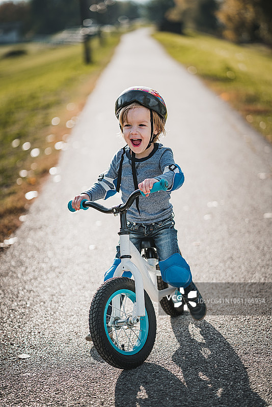 快乐的小男孩在公园里骑自行车时大喊大叫。图片素材