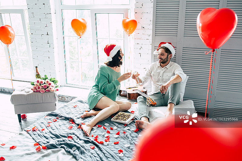 欢快和美丽的夫妇在圣诞帽庆祝圣诞和新年与香槟在浪漫的室内灯光卧室图片素材