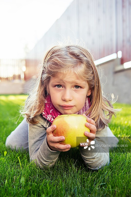 女孩拿着一个大苹果，坐在草地上图片素材