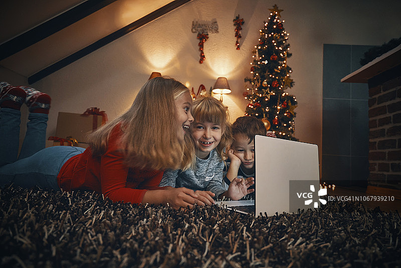 在舒适的圣诞气氛中，孩子们在客厅里拿着笔记本图片素材