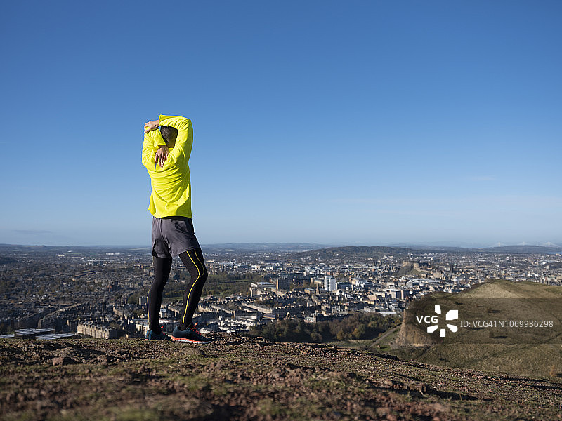 一位男性越野跑者伸展身体，欣赏风景。图片素材