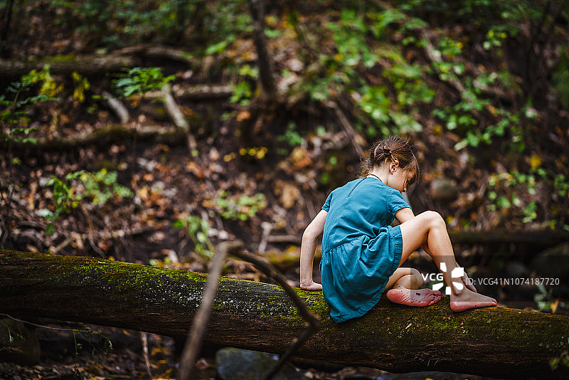 在美国的森林里，一个女孩沿着一棵倒下的树爬图片素材