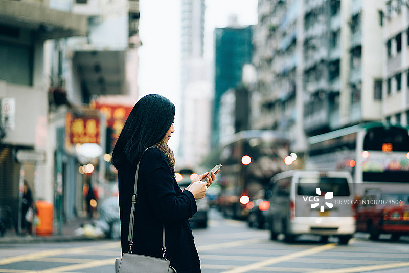 年轻女子在繁忙的交通和城市场景背景下走在市中心的街道上查看手机图片素材