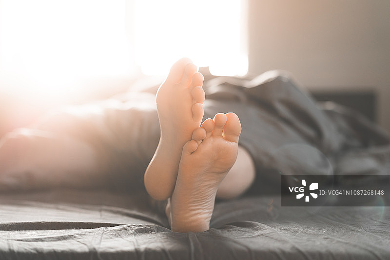 一个阳光明媚的早晨，一名妇女赤脚躺在床上图片素材