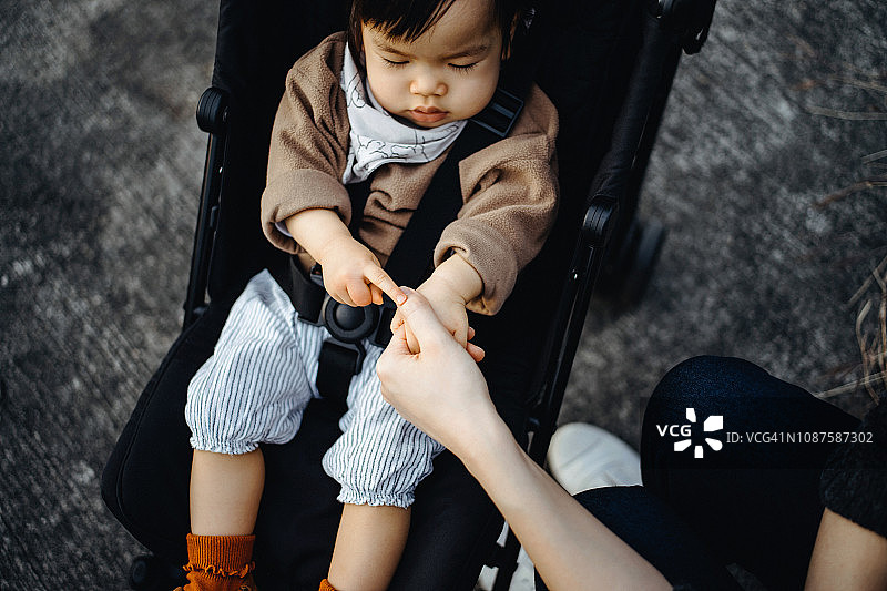 妈妈牵着坐在公园婴儿车上的小女孩的小手图片素材