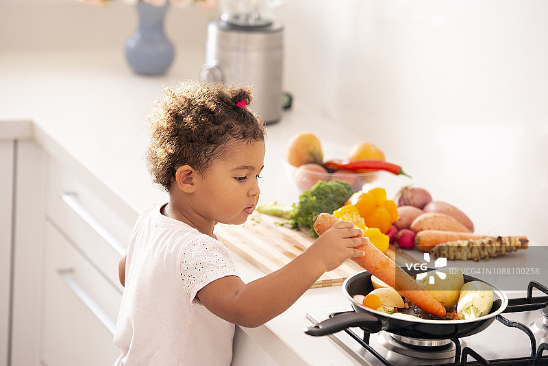 小女孩在厨房里玩蔬菜。图片素材