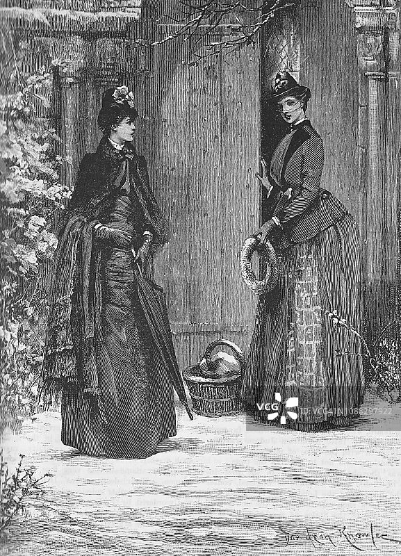 维多利亚时代的黑白版画上，两个穿着优雅的女士站在教堂的木门外，手里拿着篮子和花圈，站在雪地里;19世纪冬季装饰;箭袋1888图片素材