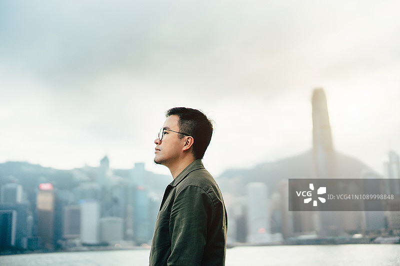 自信的年轻亚洲男子望着香港城市的景色，在一个清新明亮的早晨图片素材