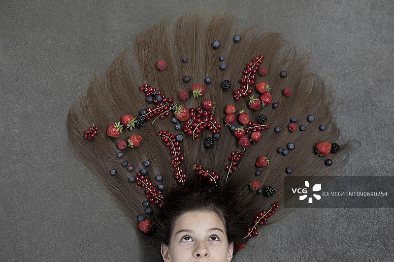 一个女孩躺在地板上，头发上有水果，向上看图片素材