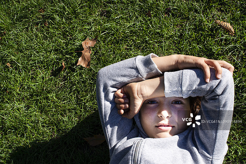 男孩在草地上用手臂挡住阳光图片素材