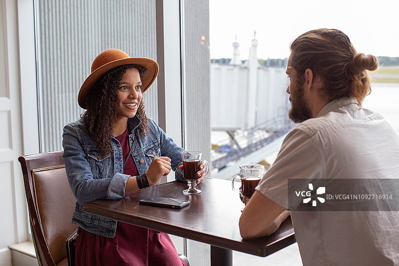 时髦的年轻跨国夫妇聊天在机场咖啡馆的咖啡。图片素材