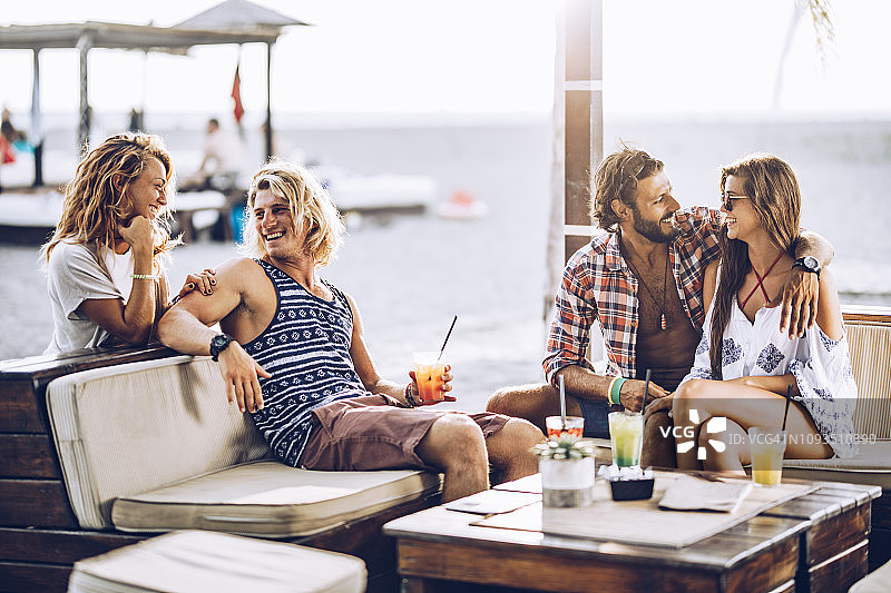 一群年轻幸福的夫妇放松在一个海滩酒吧和交流。图片素材