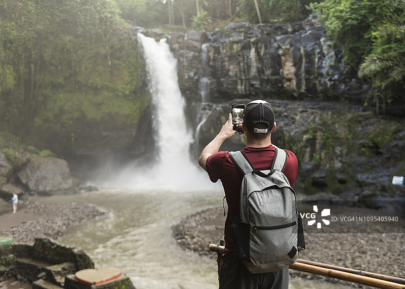 背包客在森林里用智能手机拍摄瀑布的后视图图片素材