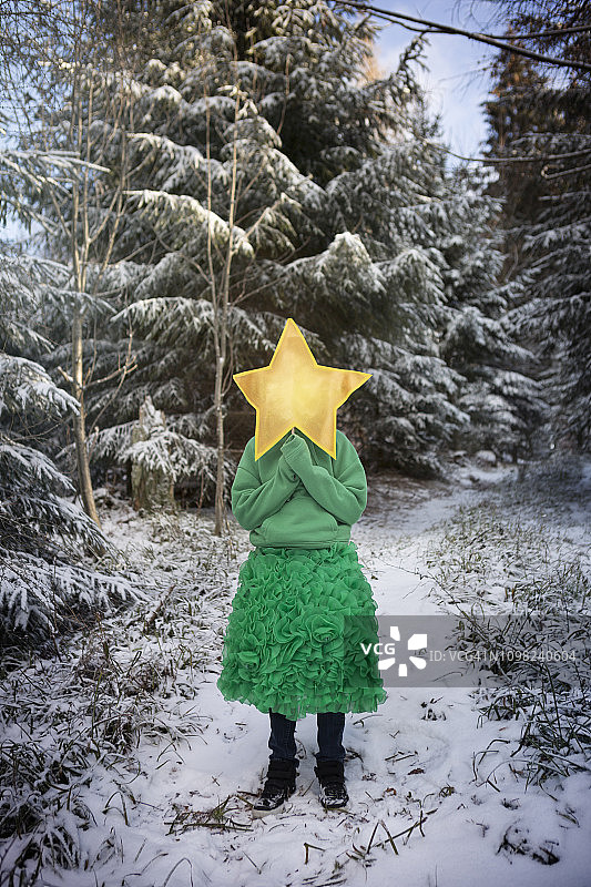 冬天的森林里，穿着绿色裙子的孩子拿着一颗黄色的星星图片素材