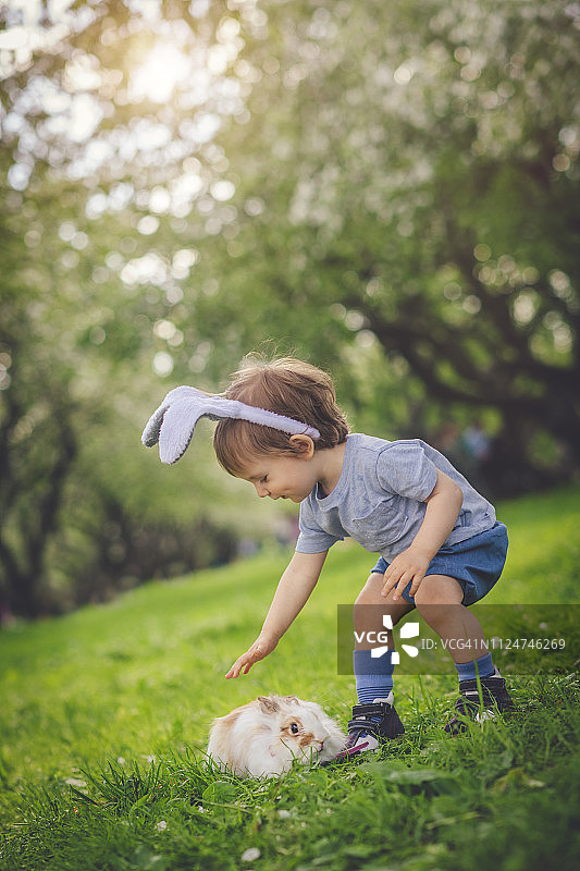 可爱的小男孩和兔子一起玩寻找复活节彩蛋的游戏图片素材