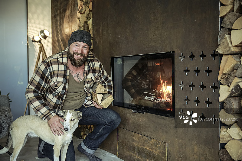 一个微笑的男人和他的狗在家里壁炉前的肖像图片素材
