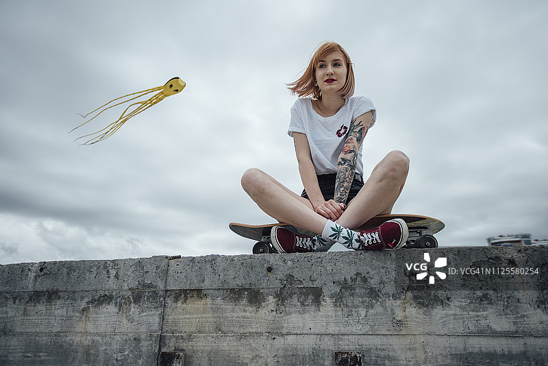 年轻女子坐在水泥墙上雕刻滑板与风筝的背景图片素材