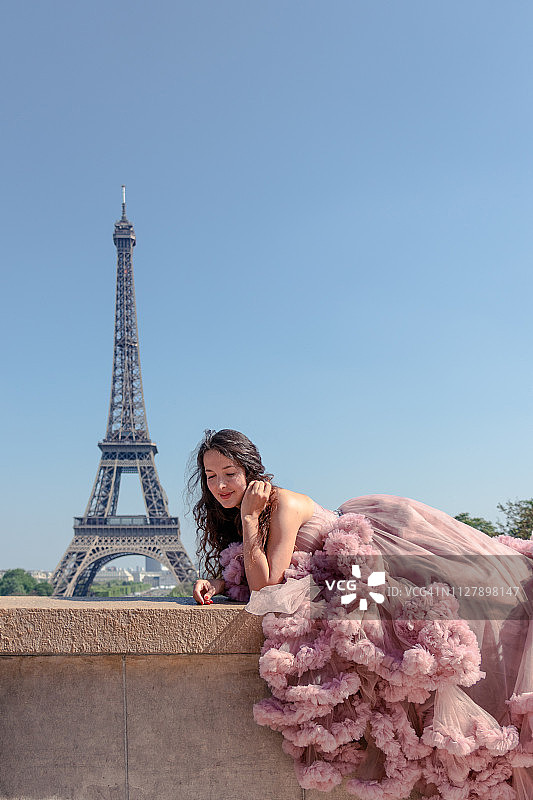 美丽的嬉皮女孩穿着一件淡粉色的舞厅礼服，以埃菲尔铁塔为背景图片素材
