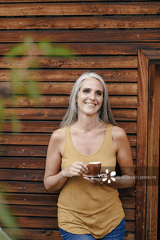 木制门面前的快乐成熟的女人与咖啡杯的肖像图片素材
