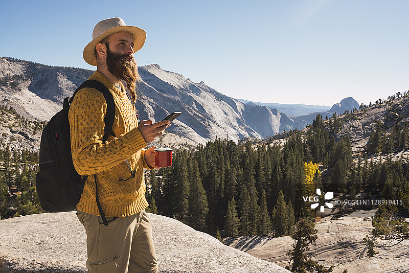 美国，加州，约塞米蒂国家公园，徒步旅行者使用智能手机和拿着杯子图片素材