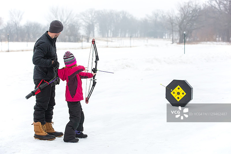 父亲和女儿在冬天户外练习射箭图片素材