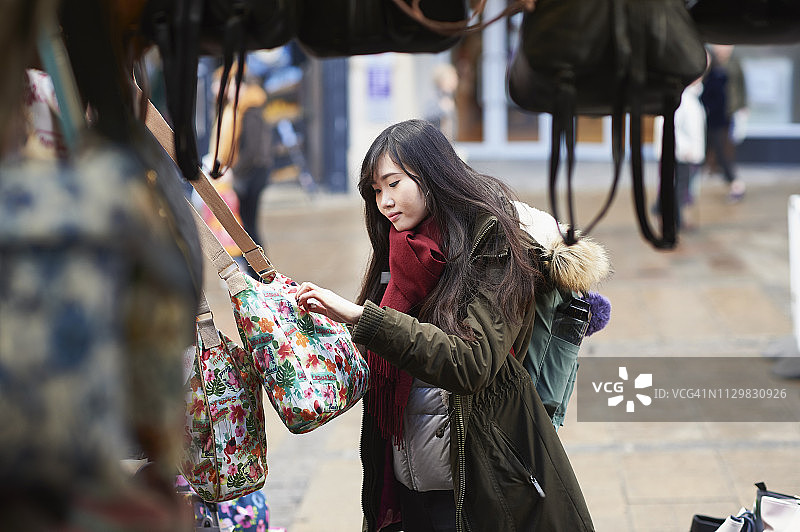 年轻女子在市场摊位上看包图片素材
