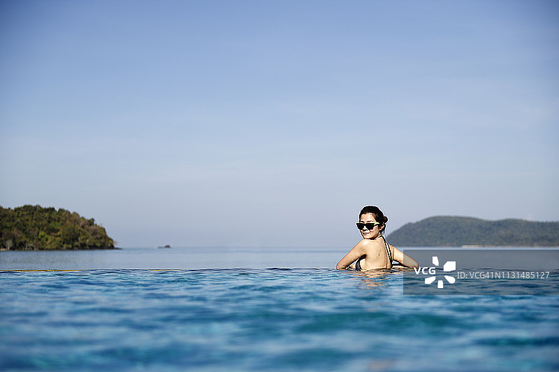 一个中国女人在俯瞰大海的无边泳池里图片素材