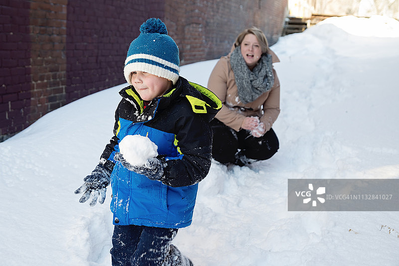 身体积极的母亲玩她的儿子在户外的雪。图片素材