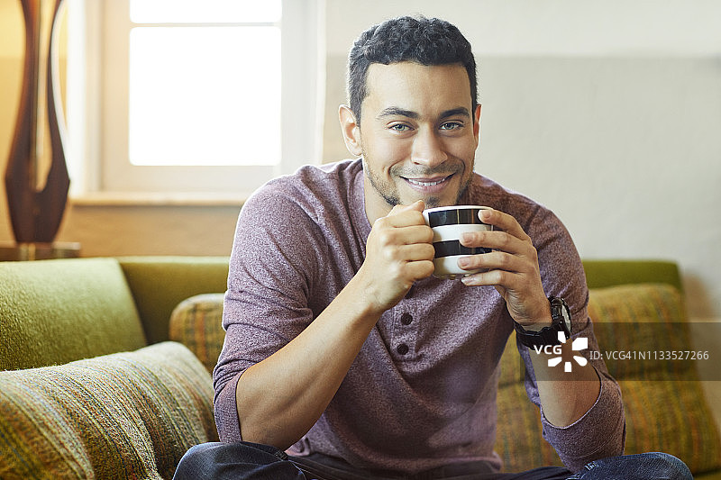 微笑的男人在沙发上喝咖啡的肖像图片素材