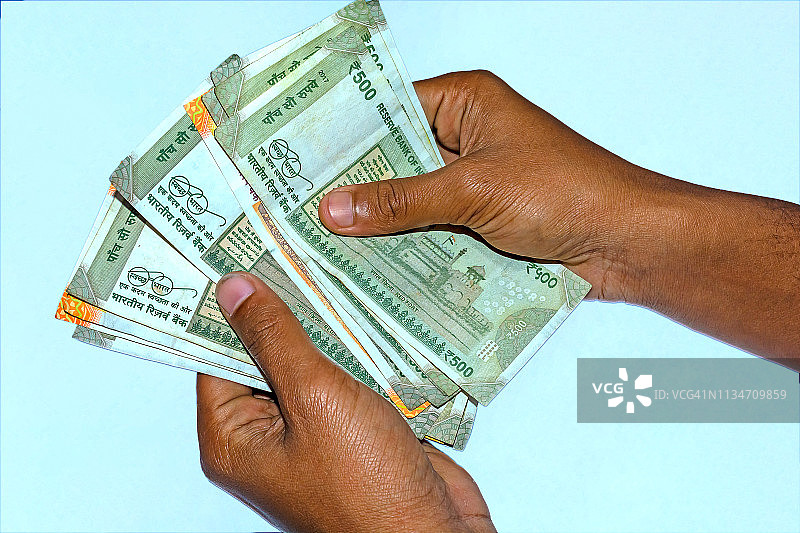 男人的手握着并数着新的500和200卢比的印度货币。图片素材