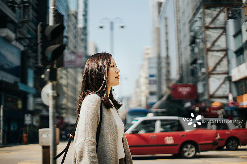 年轻女子穿过城市的街道，面对城市的摩天大楼和繁忙的交通图片素材