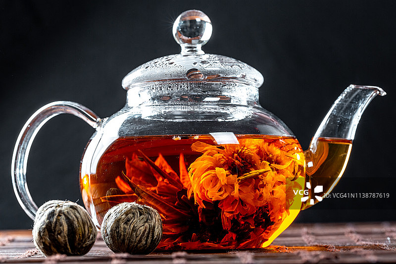 用玻璃茶壶泡茶，还有一朵盛开的大花。茶壶与异国情调的绿茶球开花。茶道上的黑色背景图片素材