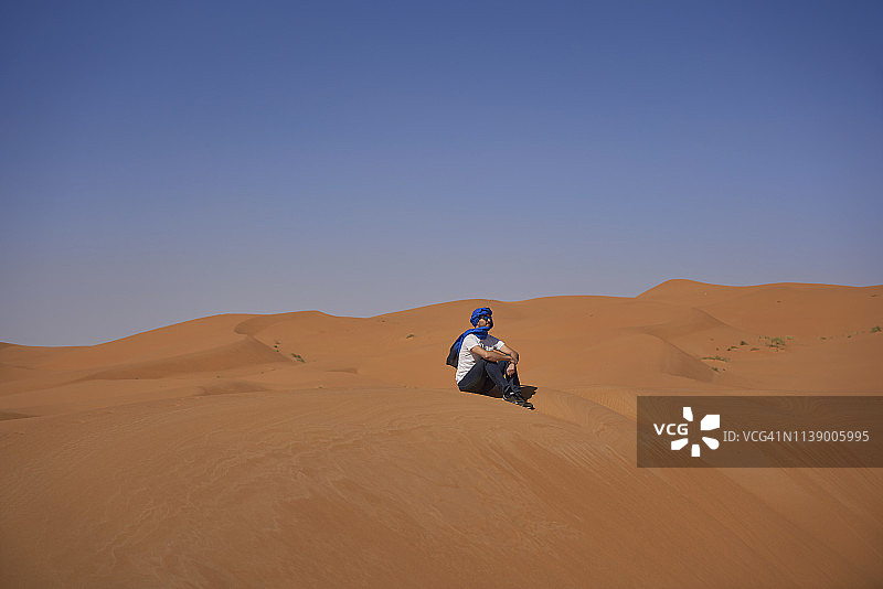 摩洛哥，一个男人坐在沙丘上看风景图片素材
