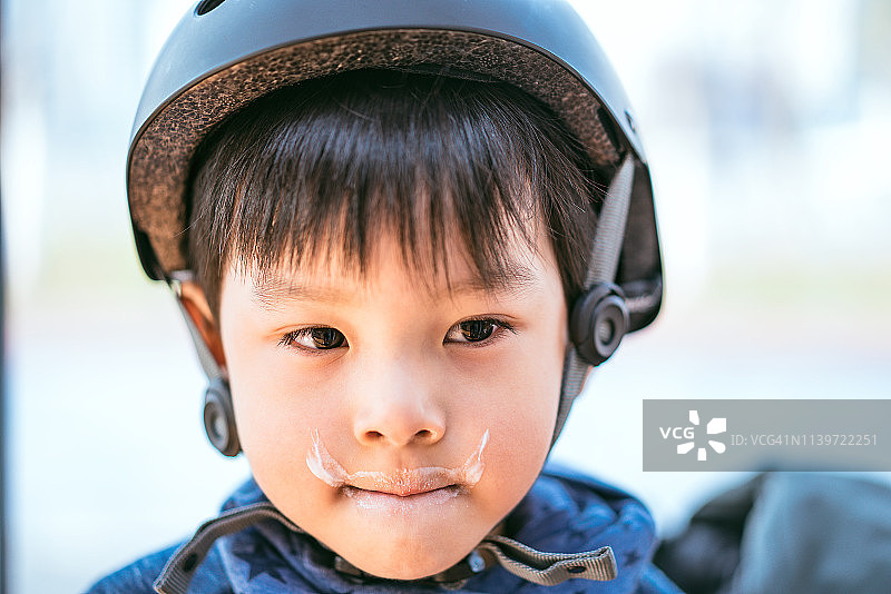 一个小男孩的特写肖像与牛奶在他的脸上和戴着运动头盔图片素材