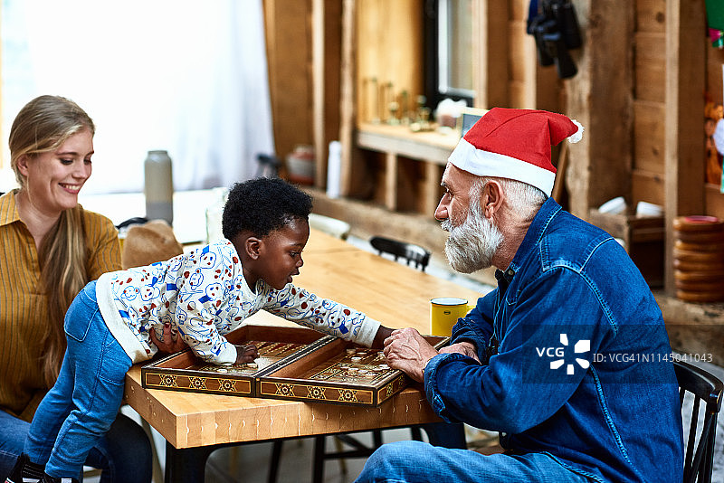 爷爷戴着圣诞老人的帽子和孙子玩棋盘游戏图片素材
