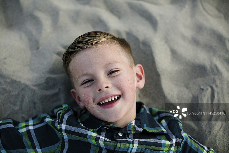 高角度肖像可爱的快乐的男孩躺在沙滩上的沙子在日落图片素材