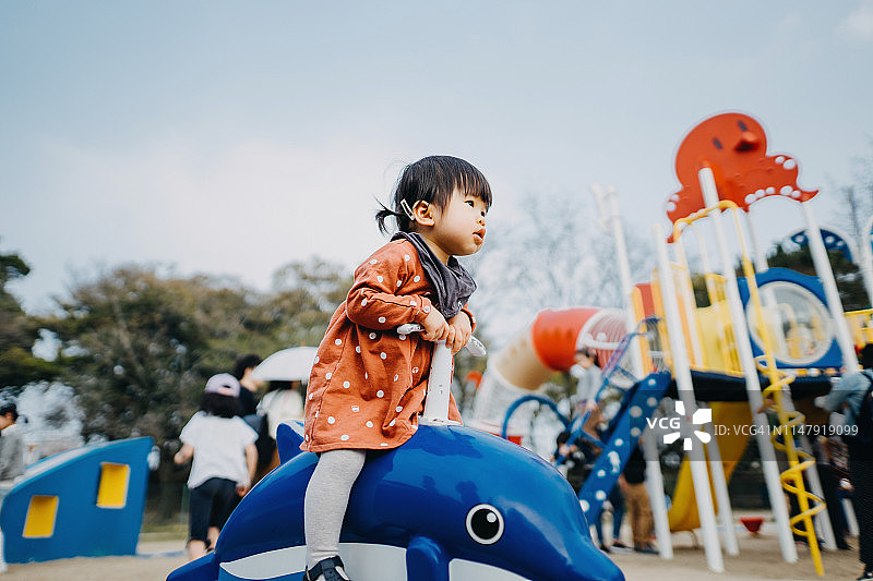 可爱的亚洲幼童女孩骑着海豚在一个可爱的阳光明媚的日子在户外操场快乐图片素材